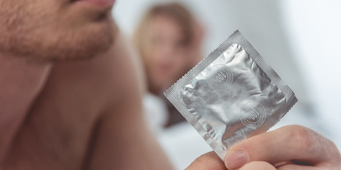 Close-up of a couple’s hands opening a delay condom packet beside a MYHIXEL box, symbolising longer, satisfying intimacy.