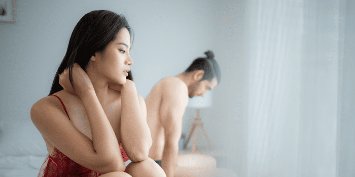 Sad couple lying in bed, faces showing sexual performance anxiety.