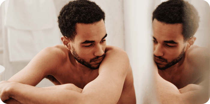 Man looking anxiously in mirror – illustration of male body dysmorphia