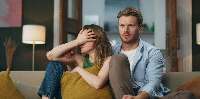 Couple cuddling on a couch, watching a horror movie together, with expressions of excitement and fear, capturing the intense emotions that can impact intimacy and connection.