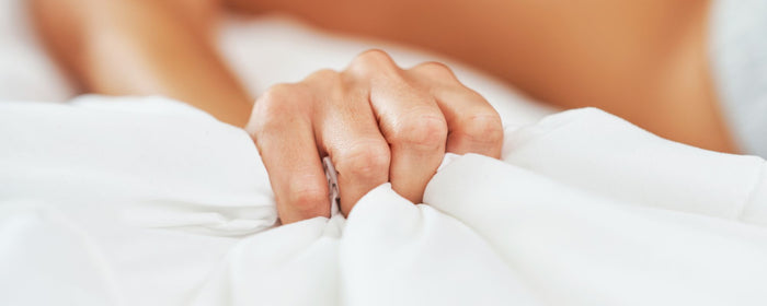 a man reaching climax in bed behind white sheets