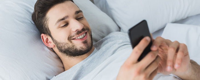 a man smiling at his phone in his bed