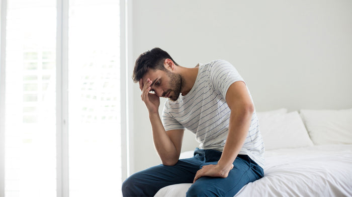 Man sitting on the edge of a bed in a calm bedroom, reflecting on male sexual wellbeing
