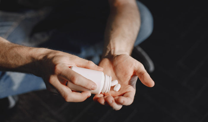 Mano vertiendo pastillas de antibiótico de un frasco, destacando los riesgos del abuso para la salud de la próstata y el equilibrio del microbioma.