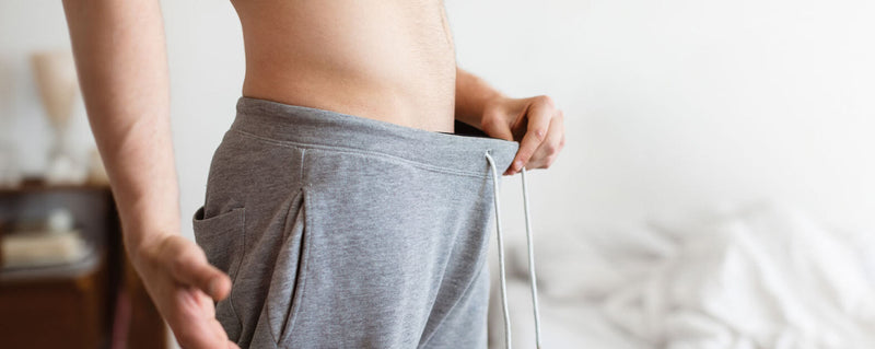 Man in winter clothes looking down at his crotch, worried that his penis shrinks in the cold