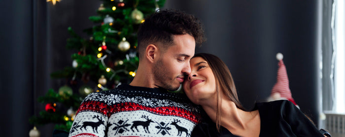 Couple exchanging a sexy Christmas gift on the sofa, smiling and cuddling.