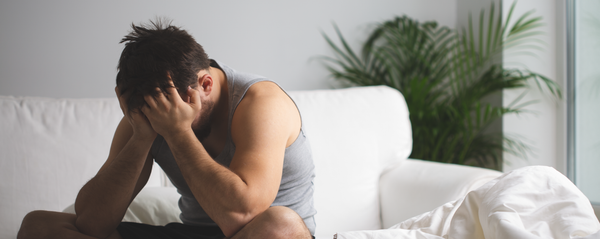 Man sitting on the edge of a bed in a thoughtful moment, representing curiosity and emotional presence in sexual wellness
